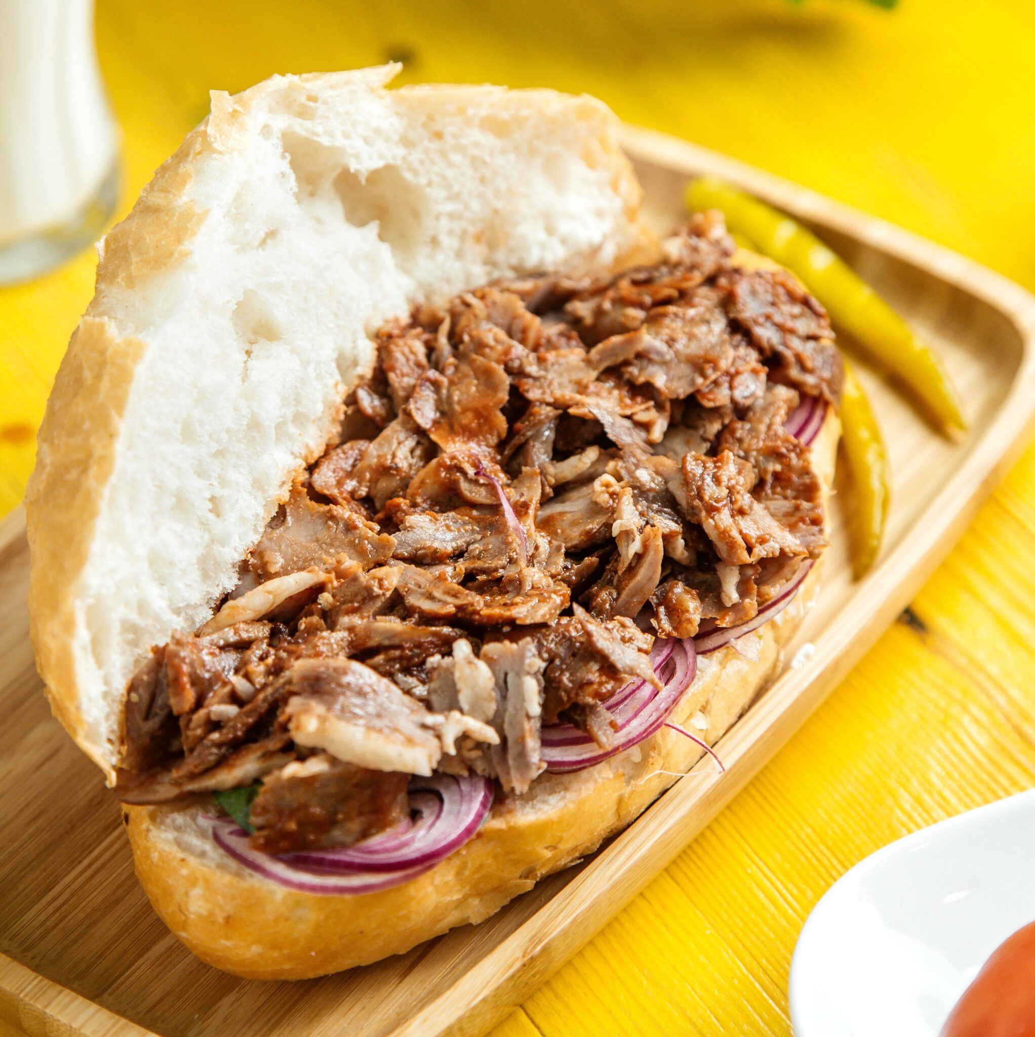 side view of beef doner in bread with pickled green pepper on a wooden platter